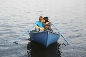 Loving young couple cuddling in rowboat at lake