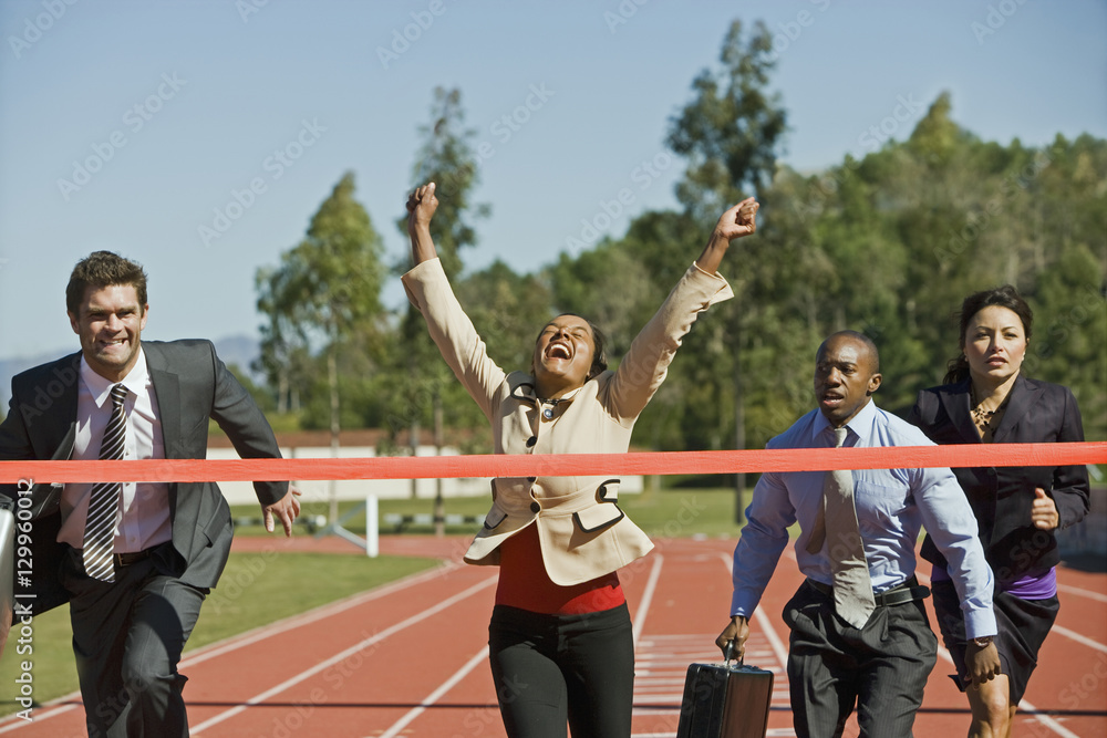 Wall mural happy businesswoman crossing the finish line while competitors running behind