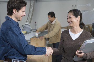 Multiethnic man and woman shaking hands in distribution warehouse