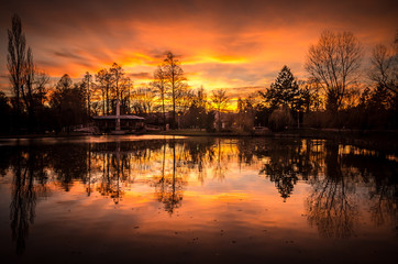 Fototapeta na wymiar Spectacular sunset with clouds in the sky. Beautiful sunset over a lake in the city park.