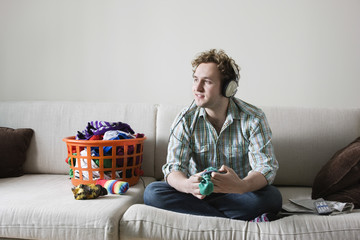 Full length of young man listening music while folding laundry on sofa