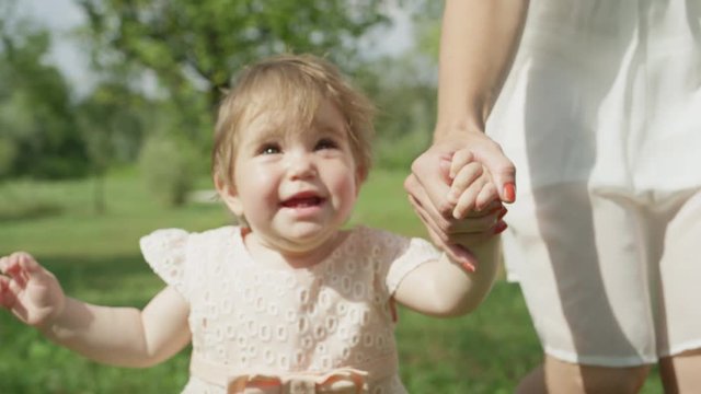 CLOSE UP SLOW MOTION: Sweet baby girl walking in park, holding hands with mother
