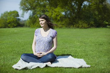 Naklejka na ściany i meble Full length of a pregnant woman sitting on grass at park