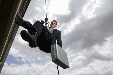 Low angle view of a spy rappelling with suitcase against cloudy sky