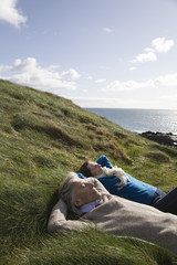 Fototapeta na wymiar Middle aged couple lying with hands behind head on coastal landscape