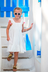 Adorable girl in white dress at street of typical greek traditional village with white walls and colorful doors in Greece