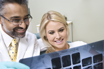 Fototapeta premium Happy dentist with female patient looking at x-ray report at clinic