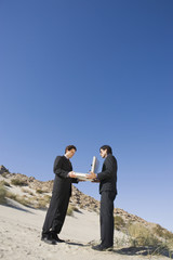 Two multiethnic business men holding open briefcase in the desert