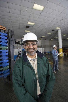 Portrait of a smiling man with colleague in the background at factory