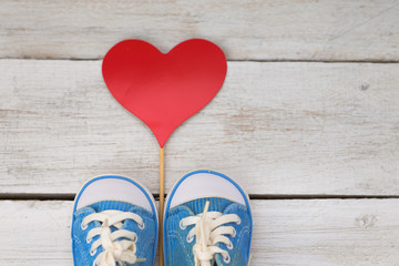baby blue sneakers on a white wooden background and red heart