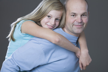 Portrait of a daughter embracing father from behind against gray background