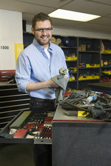 Portrait of a smiling young man with tools working in workshop