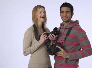 Portrait of cheerful young woman and man with digital cameras in studio