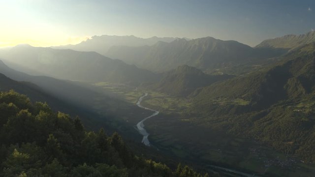 AERIAL: Mountain river running through beautiful green valley in misty evening