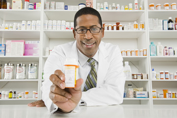 Portrait of a African American pharmacist holding out a medicine bottle