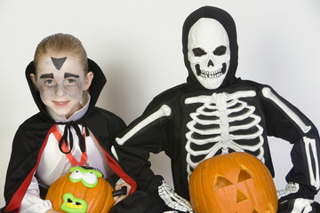Portrait of two boys dressed in Halloween costumes holding Jack-O-Lanterns isolated over white background