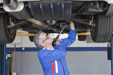 Car mechanics working below a car using a monkey wrench