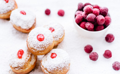 Fresh donuts (sufgania) with red jelly jam and fresh frozen cherries on a sugar powder background. Hanukkah holiday celebration and traditional jewish sweet