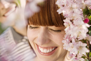Fototapeta premium Closeup of cheerful young woman with man behind blooming cherry tree