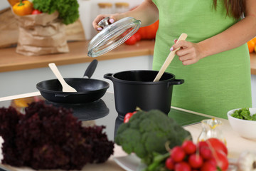 Young woman is cooking by the stove in the kitchen, close up.