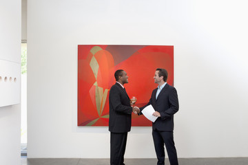 Two people shaking hands in front of wall painting