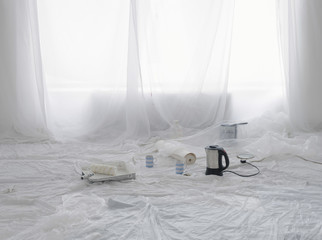 Empty room covered in dust sheets with kettle and painting supplies