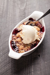 Small white aramekian bowl of boysenberry cobbler on dark wood background