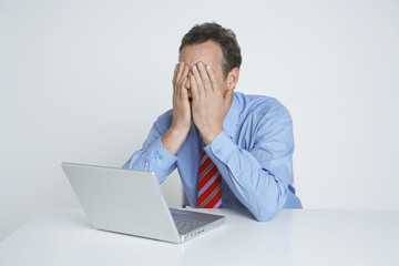 Depressed businessman with laptop at desk isolated over white background