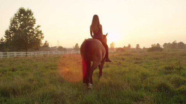 SLOW MOTION: Pretty blonde smiling girl bareback riding towards setting sun