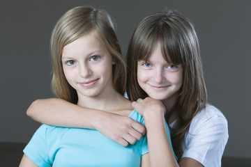 Closeup portrait of two young girls smiling against gray background