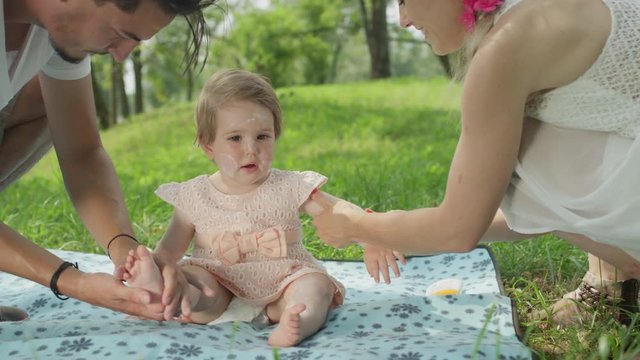 CLOSE UP: Careful young parents applying sunblock on soft baby girl's skin