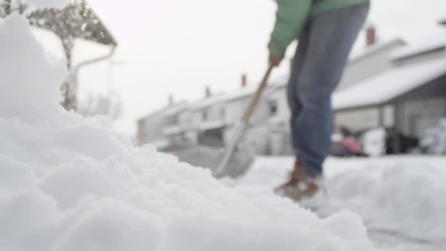 CLOSE UP: Male working, shoveling winter snow from the sidewalk, making pile