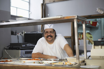 Portrait of happy middle aged male chef in standing commercial kitchen