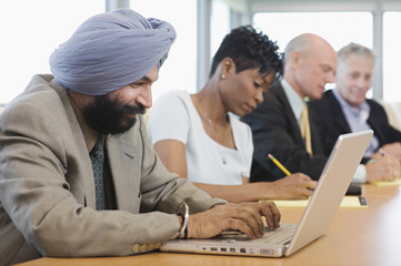 Side view of a businessman using laptop besides multiethnic colleagues in conference room