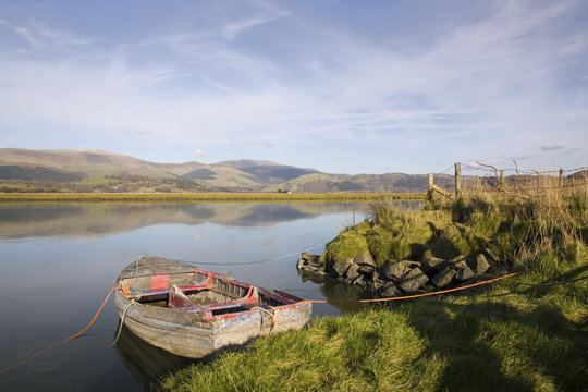 Scenic view with old rowing boat moored on bank in calm water on River Dovey (Afon Dyfi) looking north in low winter sunlight, Glandyfi, Ceredigion, Dyfed, Wales
