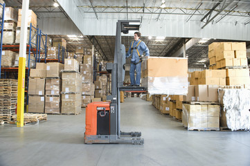 Full length of a man operating forklift truck in distribution warehouse
