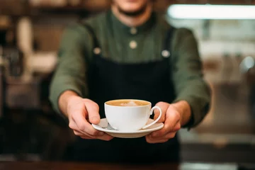 Tuinposter Waiter in black apron stretches a cup of coffee © Nomad_Soul