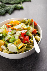 Angled shot of large white porcelain bowl of pasta and roasted vegetables on dark wood
