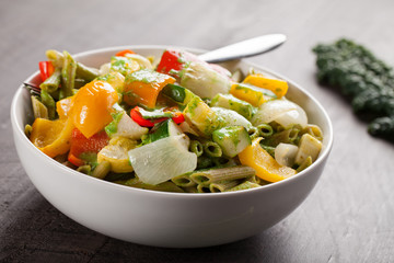 Horizontal view of large white porcelain bowl of pasta and roasted vegetables with a creamy kale sauce
