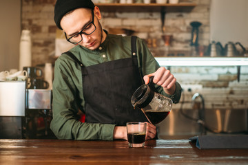 Barman pours coffee in a glass.