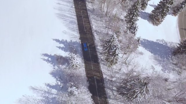 AERIAL: Blue car driving around sharp bend in magical snowy winter wonderland