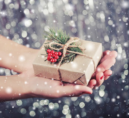 Female hands holding Christmas gift box with branch of fir tree, shiny xmas background. Holiday gift and decoration. Toning