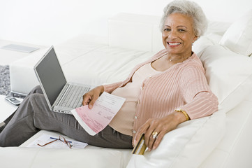 Portrait of happy African American senior woman making online payment of bills using laptop at home