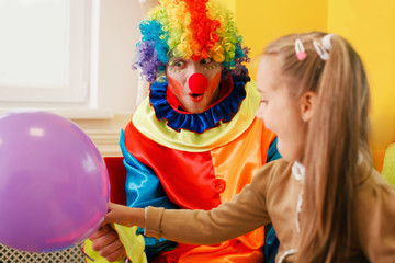 Amusing clown give air balloon to the little girl