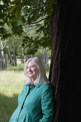 Smiling thoughtful middle aged woman standing beneath a tree