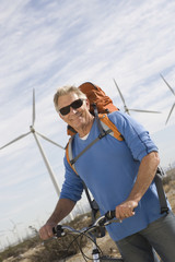 Portrait of a happy senior man with bicycle and backpack at wind farm