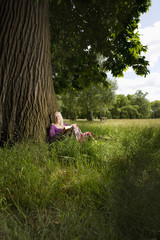 Middle aged woman sitting beneath a tree with book