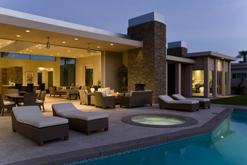 Spacious house exterior with sunloungers on patio by swimming pool at dusk