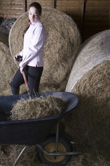 Young woman shoveling hay in barn © MDBPIXS