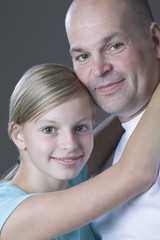 Young daughter embracing her father against gray background